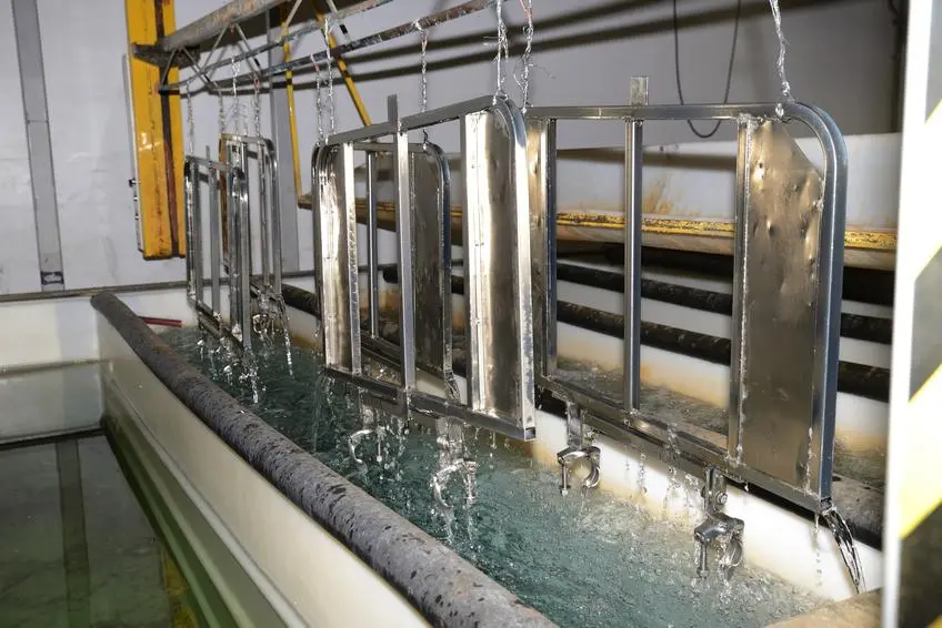 Metal parts undergoing electroplating process on racks inside a plating tank